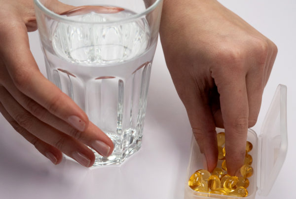 hand holds a glass of water while grabbing a yellow vitamin from a plastic container